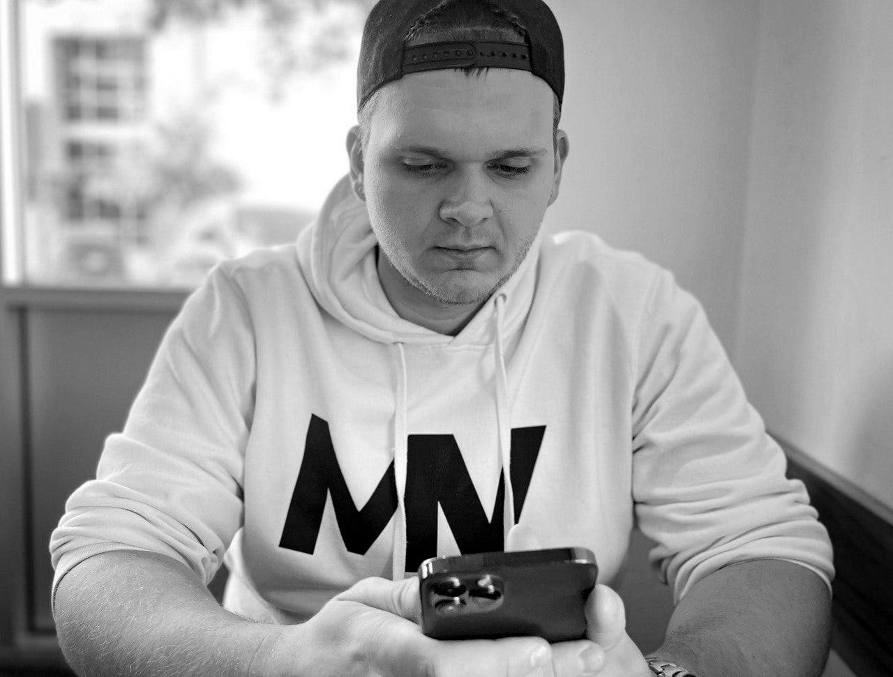 Isaac Mashman in a white hoodie, looking at his phone in a coffee shop in Little Rock
