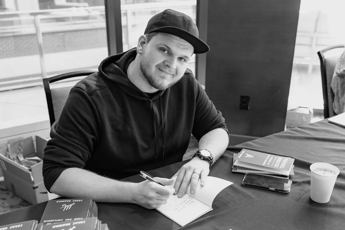 Isaac Mashman at the signing table after his presentation in Denver, pen in hand, an open copy of the Manifesto in front of him