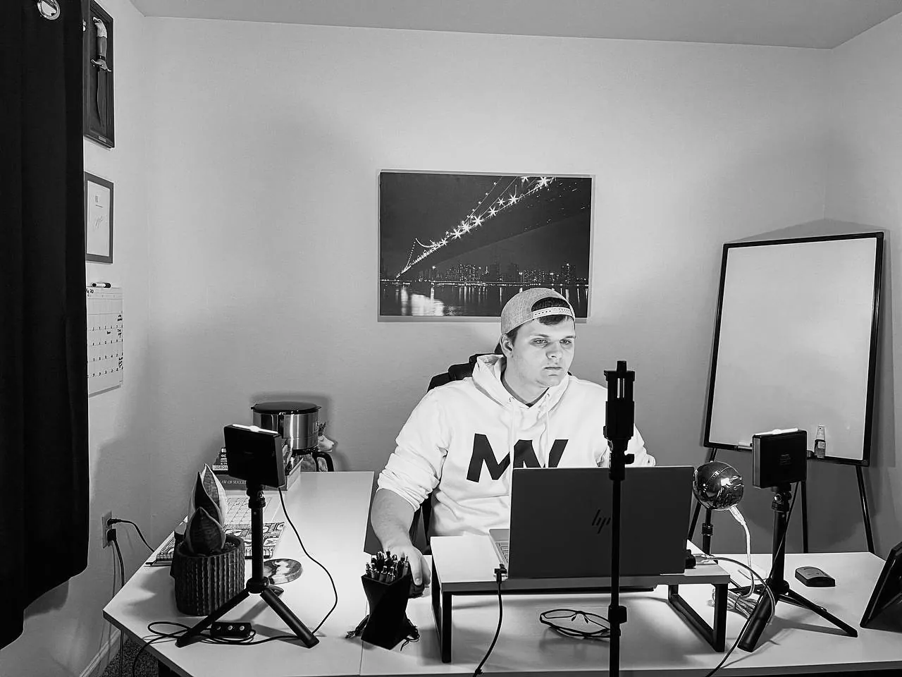 Isaac Mashman at his desk in a home office lit for video, in a Mashman Ventures hoodie, a whiteboard and cameras around him