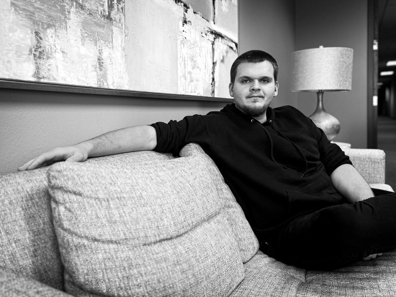 Isaac Mashman seated on a grey sofa in a black hoodie