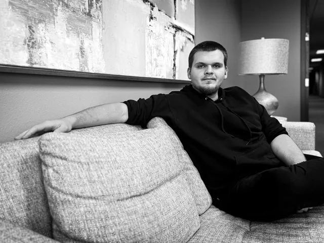 Isaac Mashman seated on a grey sofa in a black hoodie