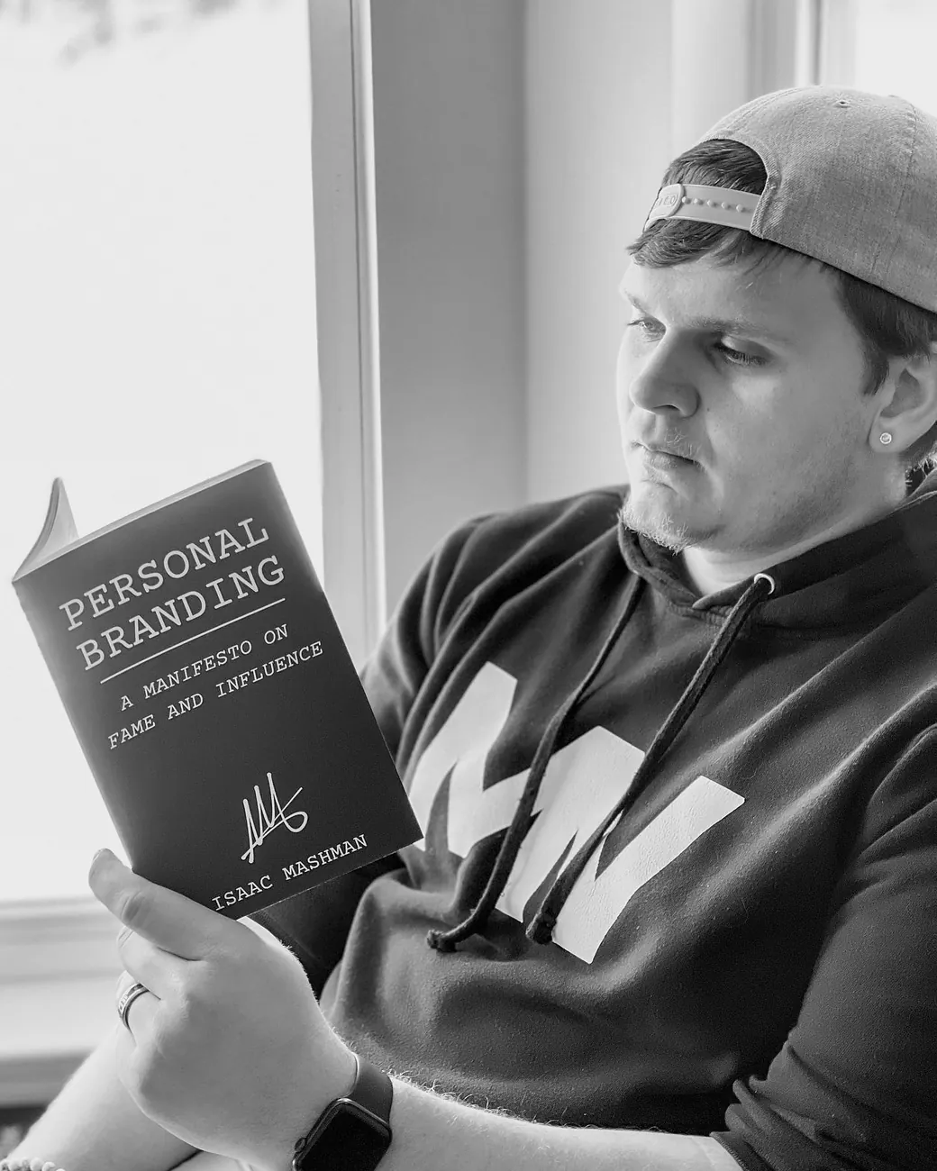 Isaac Mashman reading the First Edition of the Manifesto by a window, in a Mashman Ventures hoodie and a backwards cap