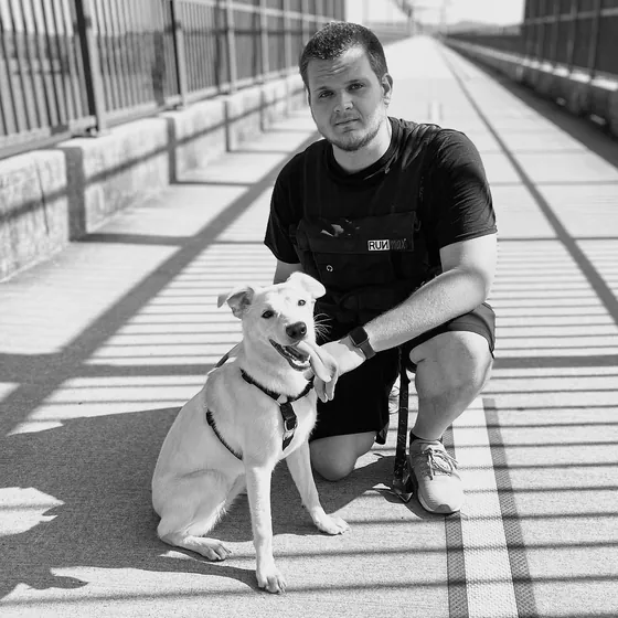 Isaac Mashman kneeling on a bridge walkway in a weighted vest, beside a white dog